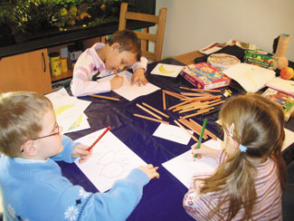 3 Kinder lernen am Tisch mit Zettel und vielen Stiften